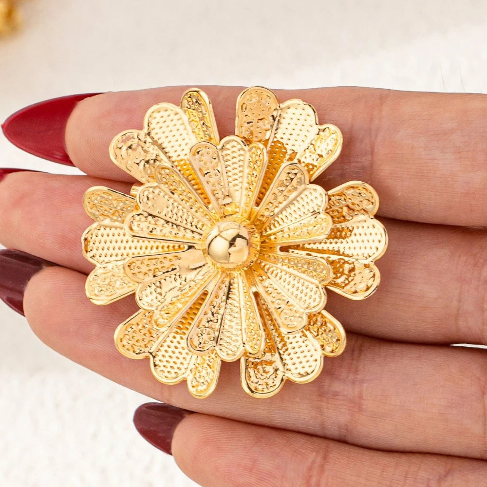 Gold floral brooch held between fingers with a white background