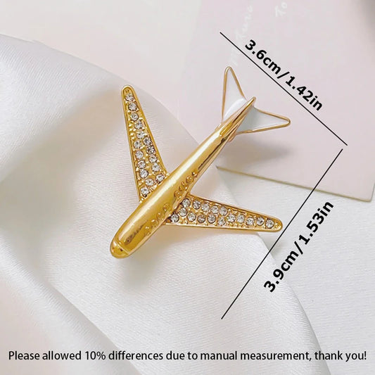 Gold airplane shaped brooch with rhinestones and size measurements on white fabric background