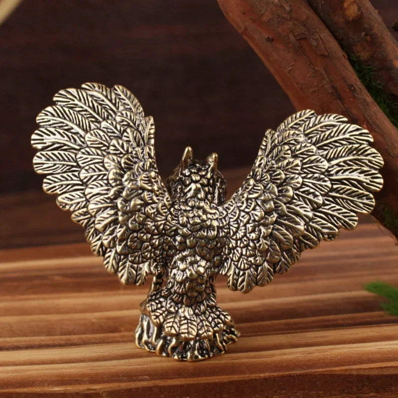 An ornate metallic owl figurine with outstretched wings, shown in a textured antique silver finish on a wooden surface.