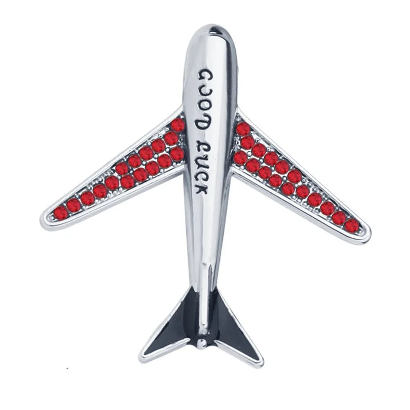 Airplane brooch with red crystal accents and Good Luck text on white background.