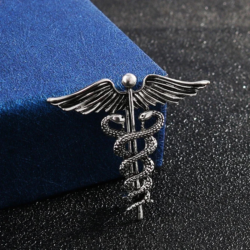 Silver caduceus brooch on a blue cushion with a dark textured background