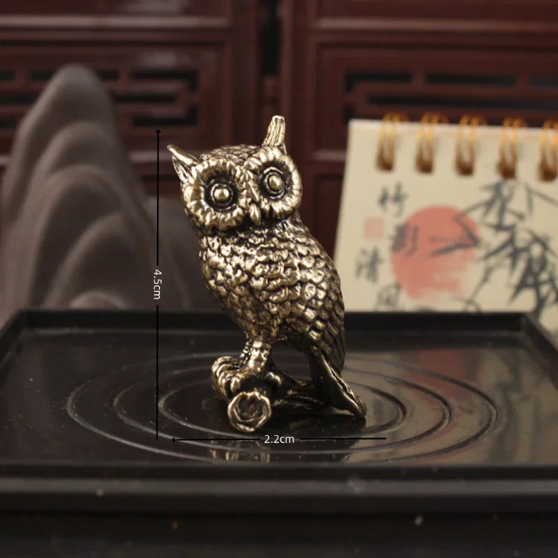 A small metallic owl figurine with a textured, antique bronze finish, shown standing on a black tray. Black dimension lines overlay the image, indicating a height of 4.