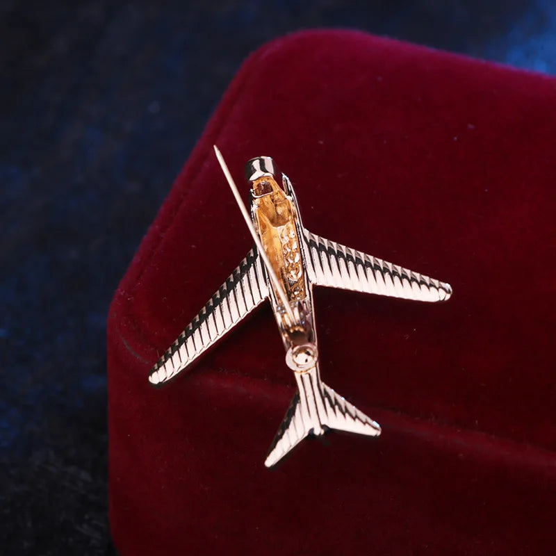 Gold airplane brooch pin displayed on a luxury red cushion.
