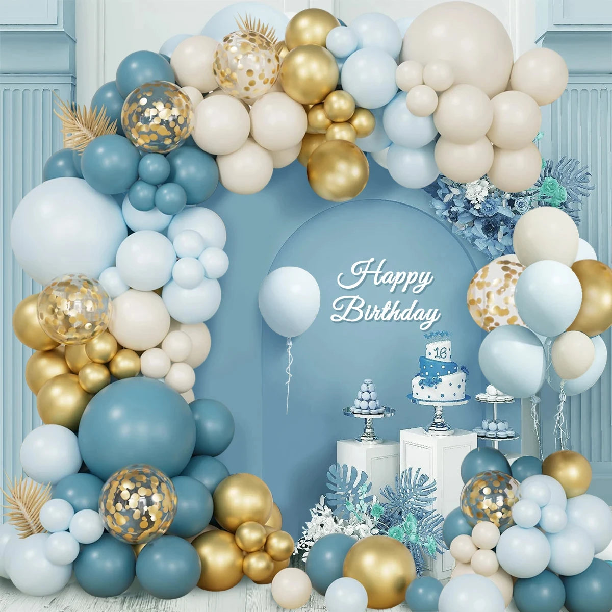 A large balloon garland arch and party decoration setup in pastel blue, cream, and metallic gold, with confetti-filled balloons, decorative foliage, a small cake stand, and the words 'Happy Birthday' on a blue backdrop.