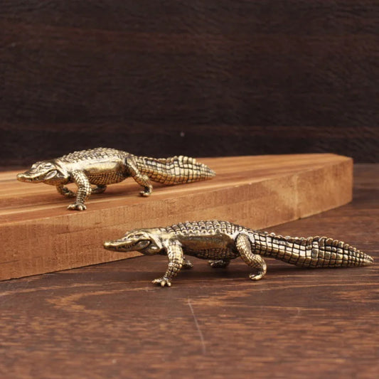 Two bronze alligator figurines on a wooden surface with a dark background