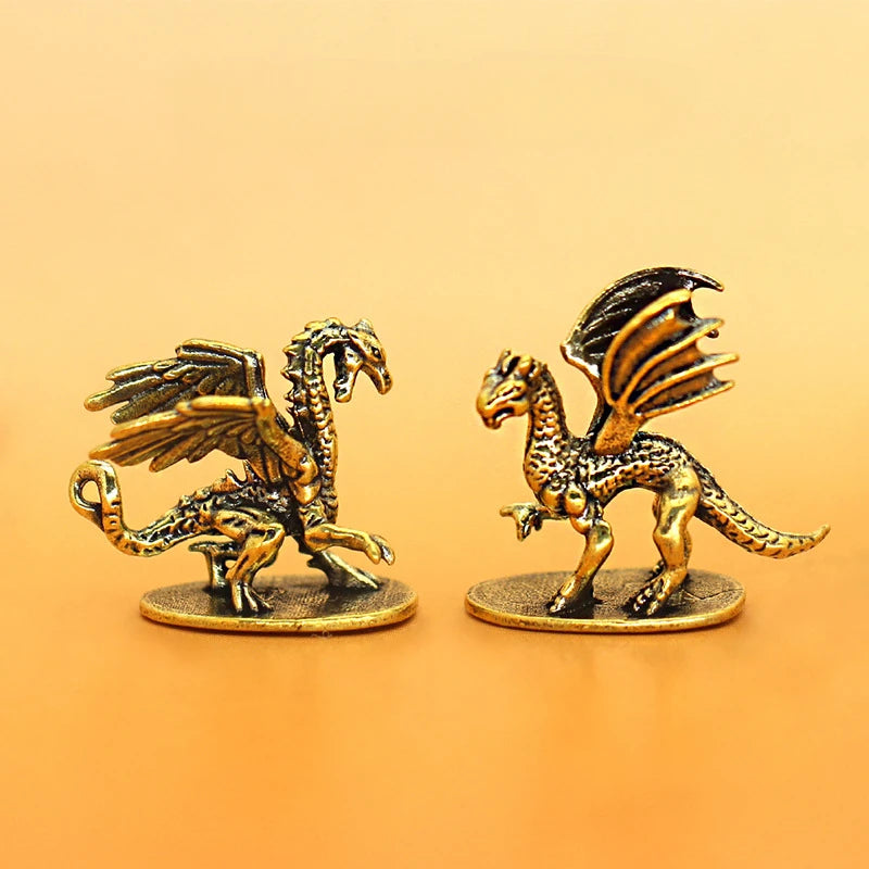 Two small metallic dragon figurines on round bases, photographed against a smooth warm gradient background. One dragon is facing left with wings spread, and the other is facing right with wings folded.