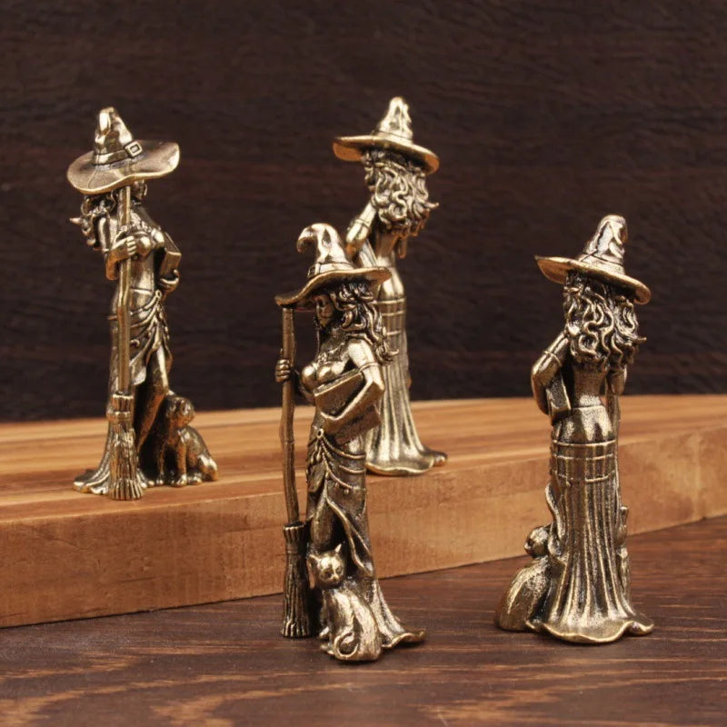 Three metallic witch figurines on a wooden surface with a dark background