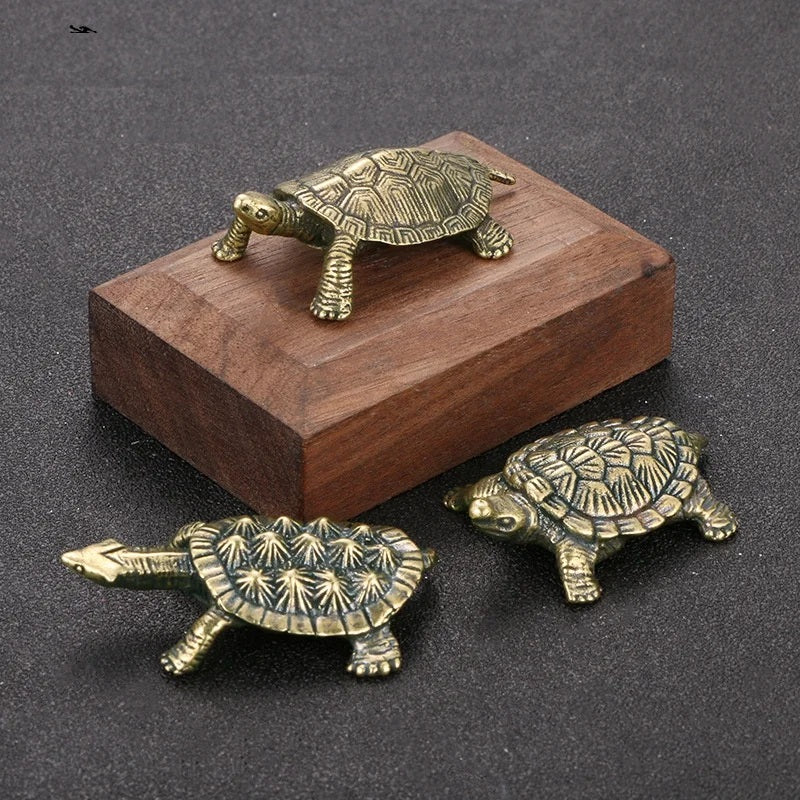 Three brass turtle figurines on a dark surface with a wooden block.