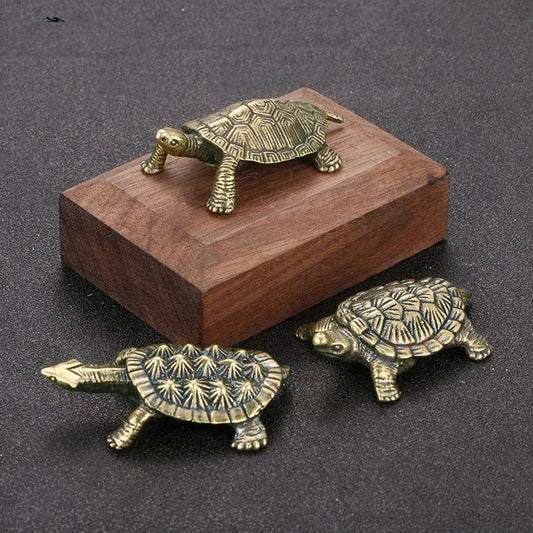 Three brass turtle figurines on a dark surface with a wooden block.
