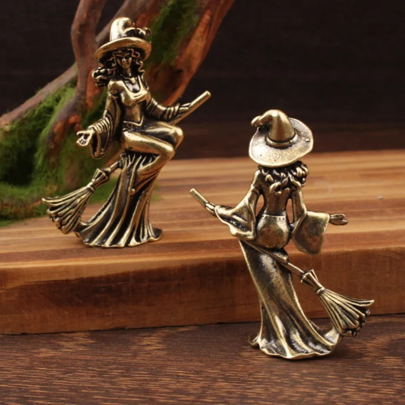 Two bronze witch figurines on a wooden surface with a natural background.