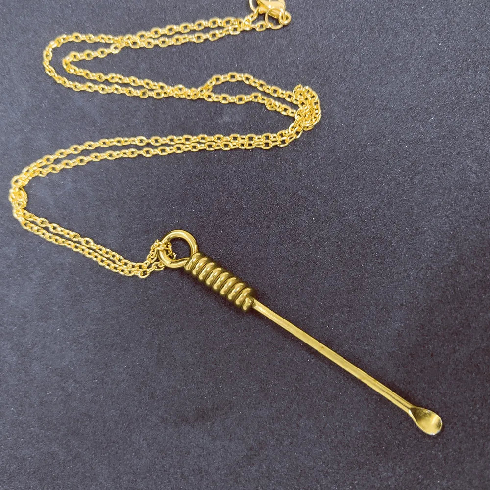 Vintage gold spoon pendant necklace with long chain displayed on a dark textured background