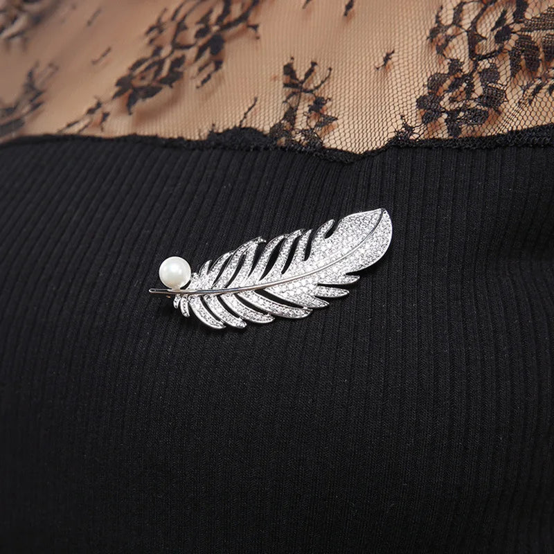 Silver feather brooch with a pearl on a black fabric background
