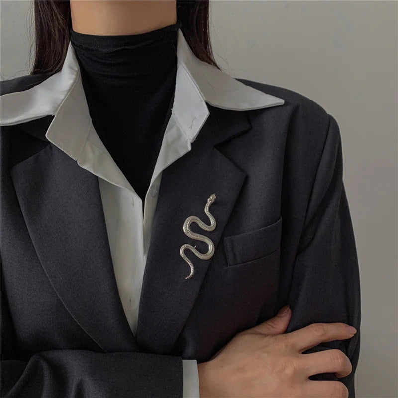 Person wearing a gold snake brooch pin on a dark blazer over a white shirt.