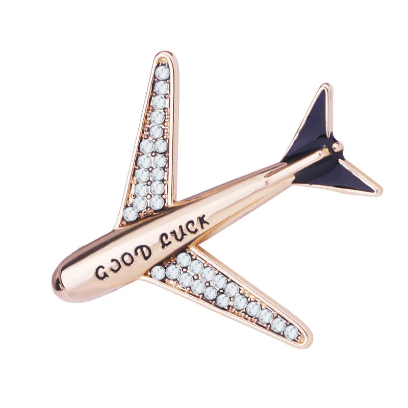 Rose gold airplane brooch with engraved Good Luck message on white background.