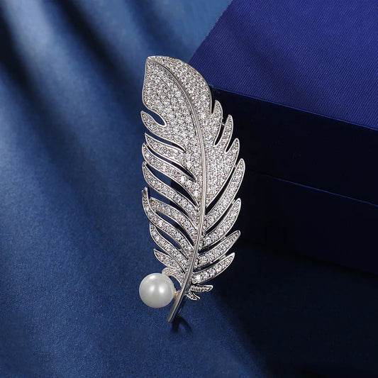 Silver feather-shaped brooch with a pearl on a blue fabric background
