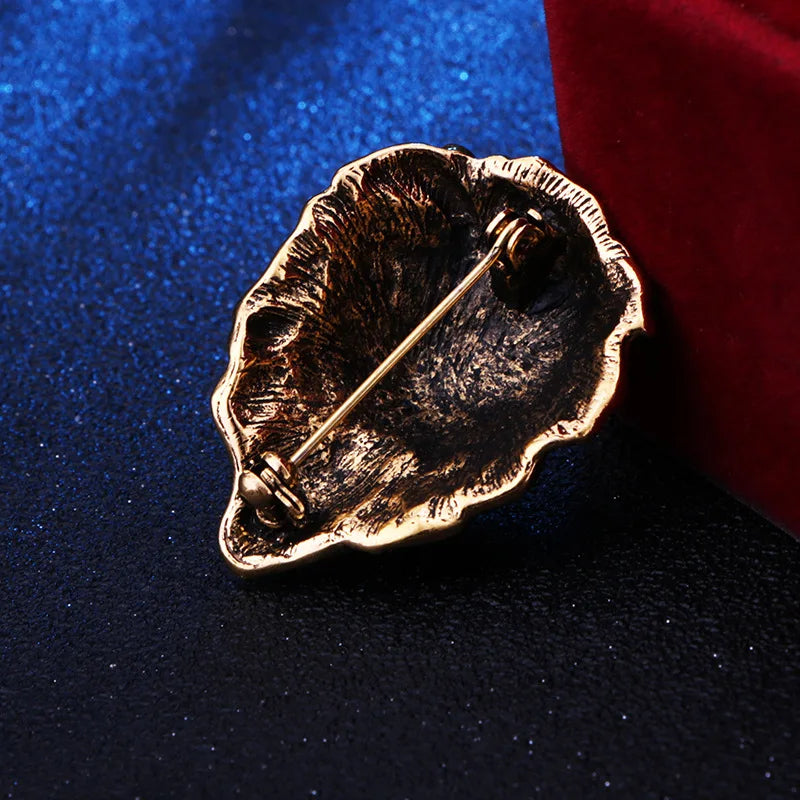 Gold leaf-shaped brooch on a dark blue and red fabric background
