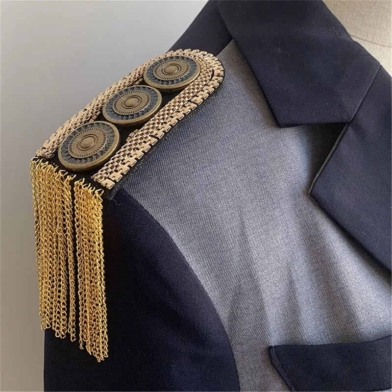 Dark blazer with gold tassel shoulder accessory on neutral background