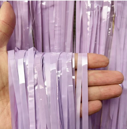 Hand holding a strip of purple tinsel against a curtain background