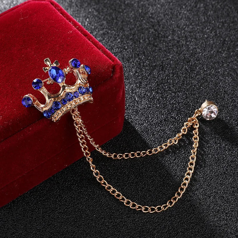 Crown-shaped brooch with blue gemstones and a chain on a dark background