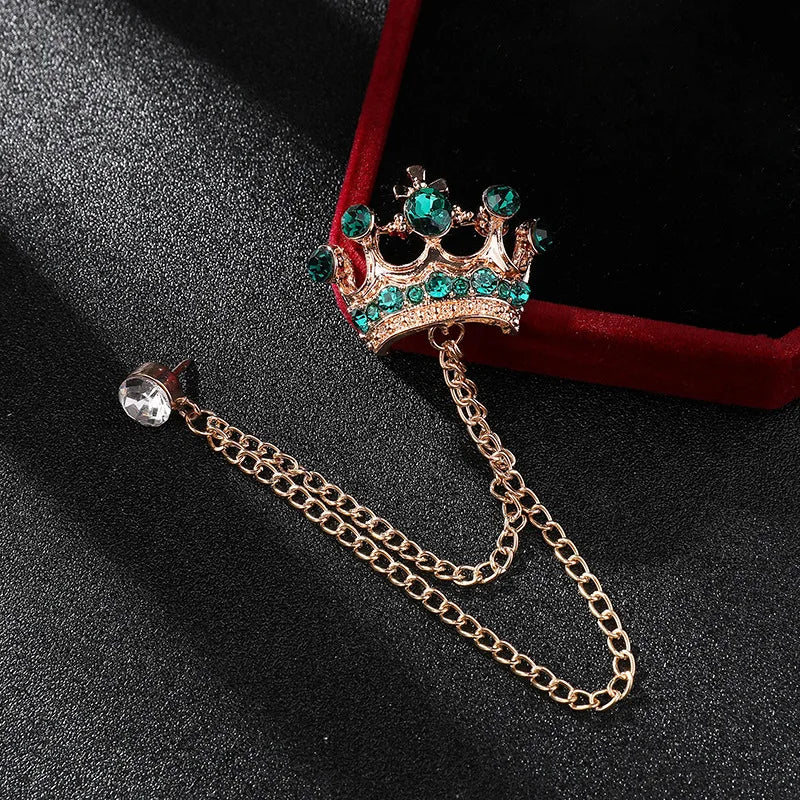 Crown-shaped brooch with green gemstones and chain on a dark surface