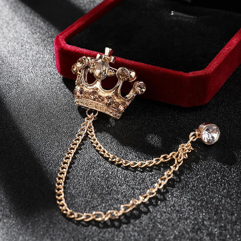 Gold crown-shaped brooch with chain and gemstone on a dark surface