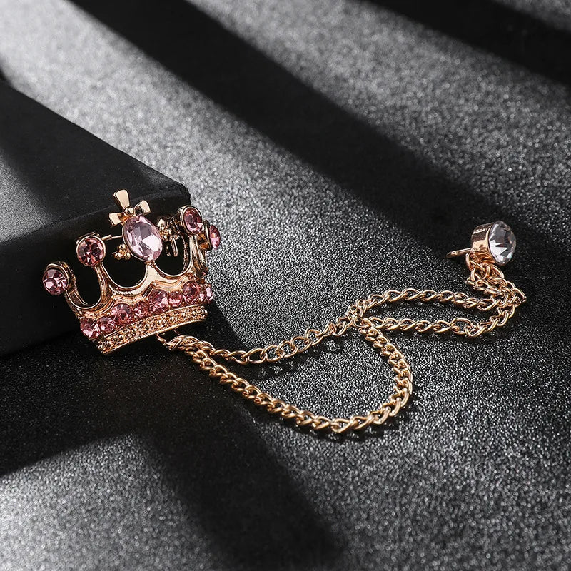 Crown-shaped brooch with pink gemstones and gold chain on a dark surface