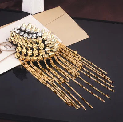 Gold spike shoulder brooch with chain tassels on black background