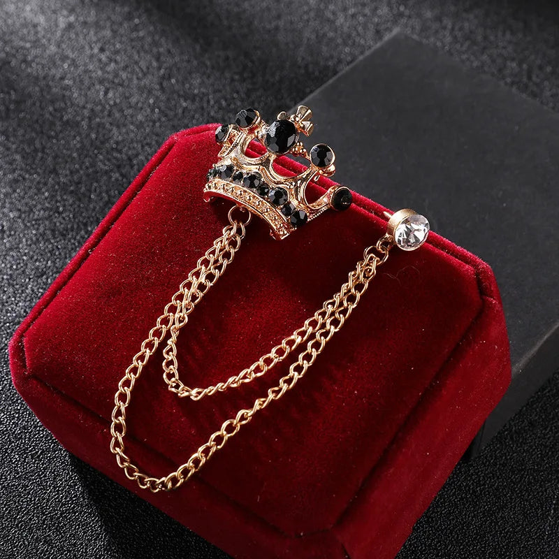 Gold crown-shaped brooch with chain on a red cushion against a dark background