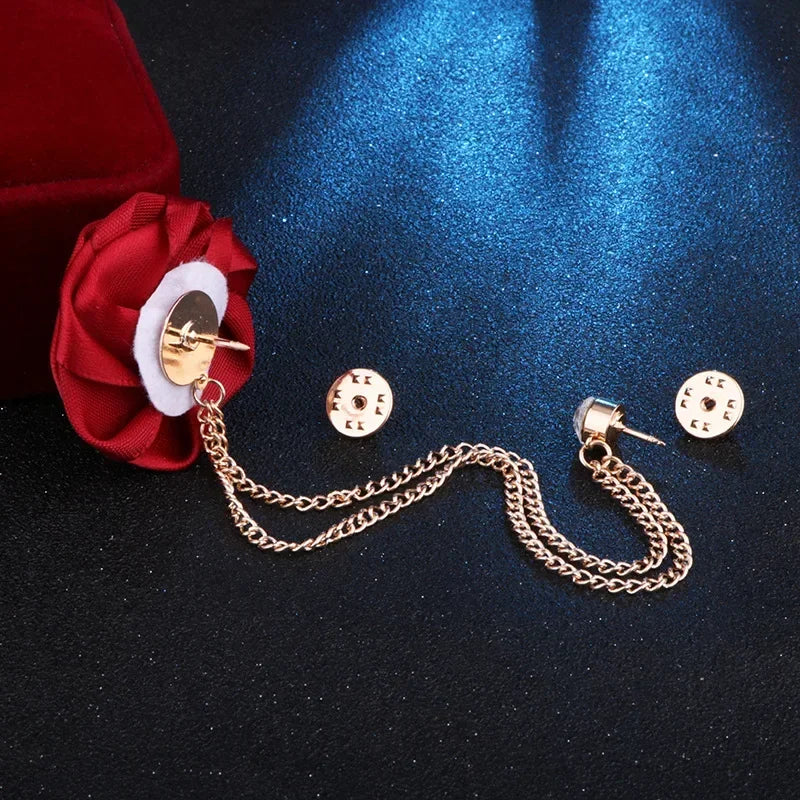 Floral lapel brooch with decorative chain displayed on dark fabric background.