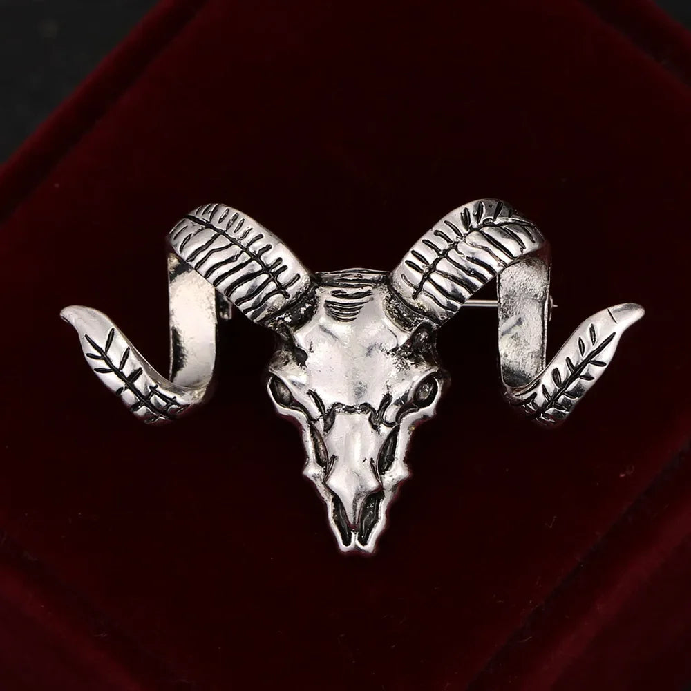 Silver ram skull brooch with detailed horn design on a dark background.