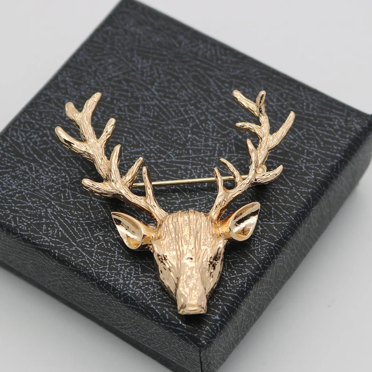 Gold deer head brooch on a textured black box