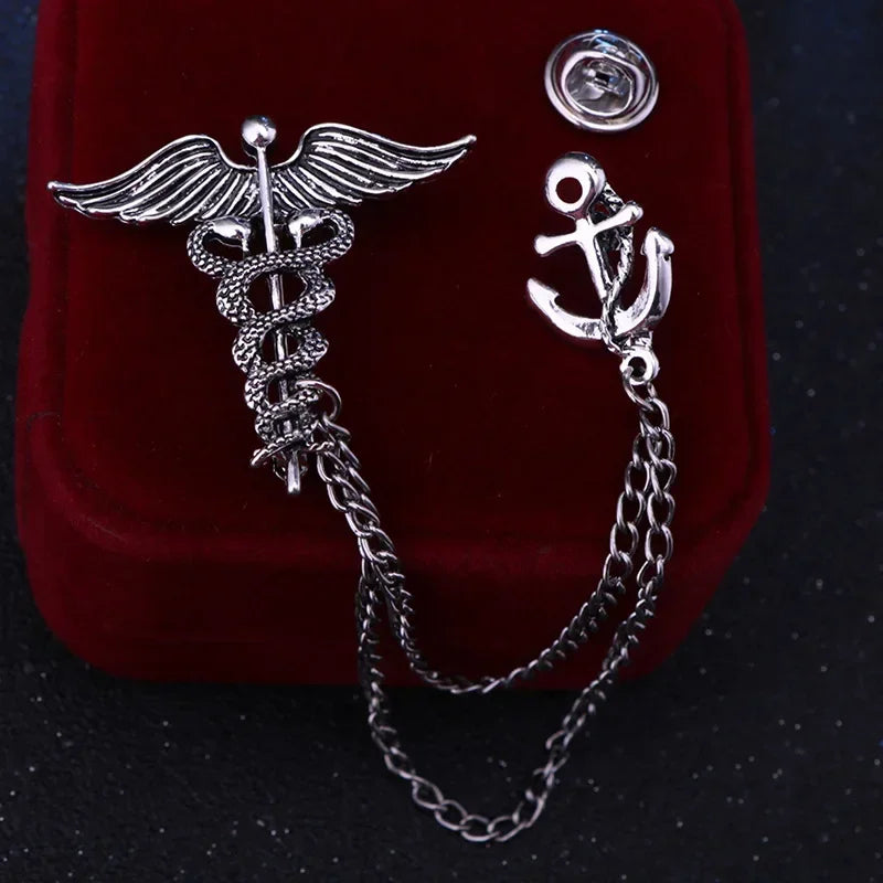Two silver pins, one with a caduceus design and the other with an anchor, on a dark background.