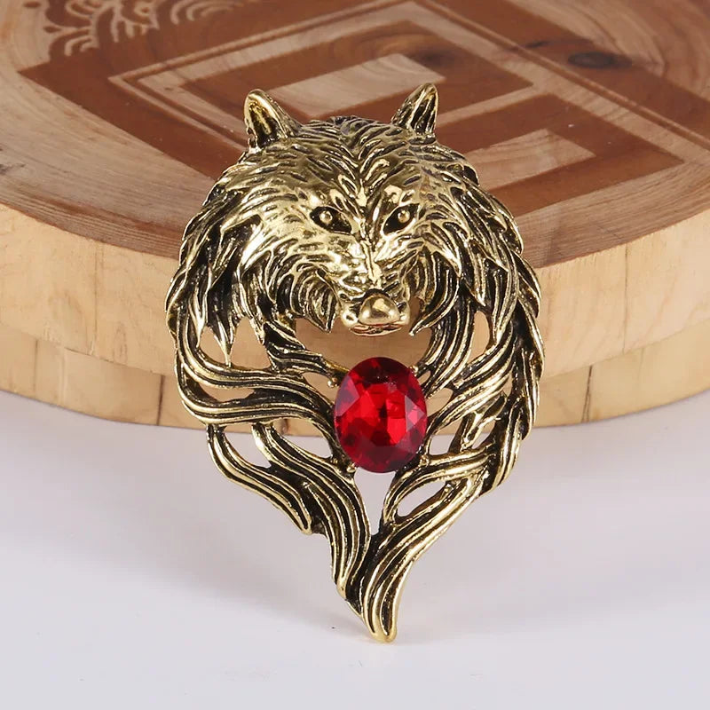 Gold wolf head brooch with a red gemstone on a wooden surface