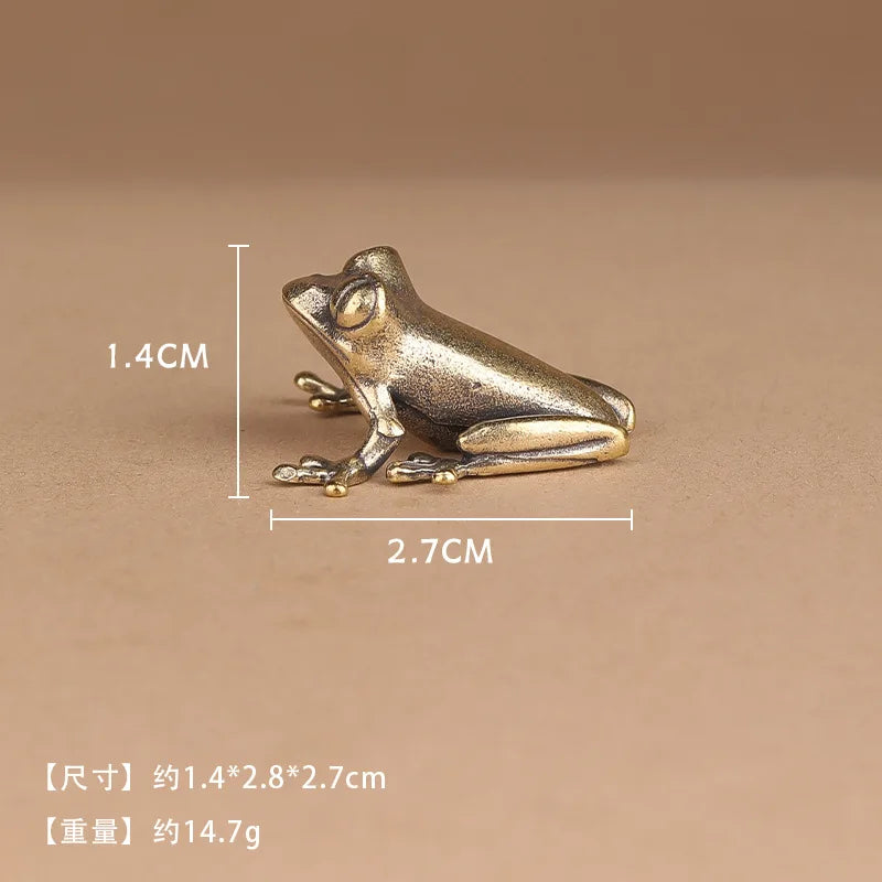 A small metallic frog figurine shown on a warm beige background with overlaid dimension lines and text indicating 1.4 cm height, 2.