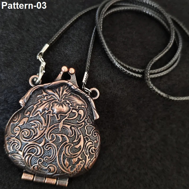 An ornate antique bronze locket pendant necklace with intricate floral and scroll engravings, shown on a black textured background with a black cord.