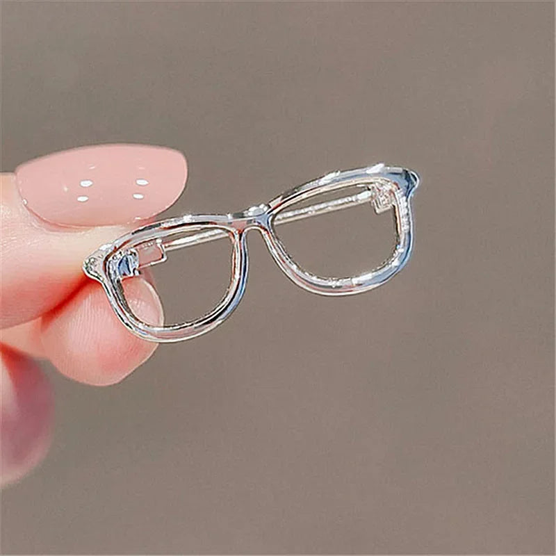 Clear eyeglasses brooch pin held by hand on plain background