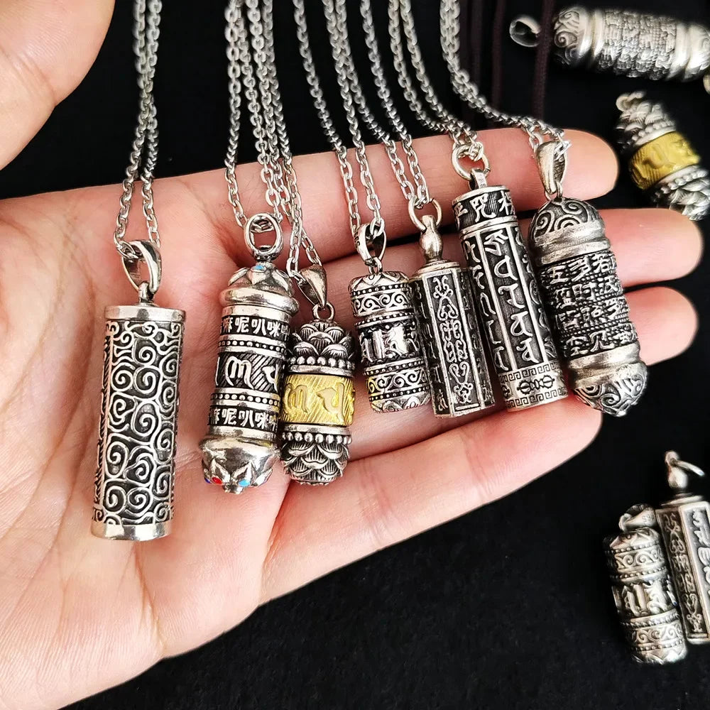 Silver prayer wheel pendants on chains held in a hand against a black background