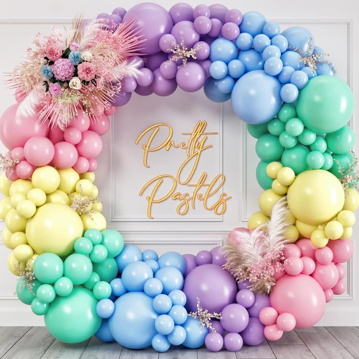 Colorful balloon arch with pastel colors and decorative flowers against a white wall.
