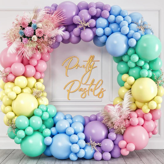 Colorful balloon arch with pastel colors and decorative flowers against a white wall.