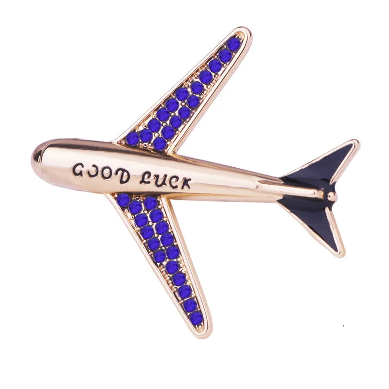 Gold airplane lapel pin with blue crystal stones on white background.