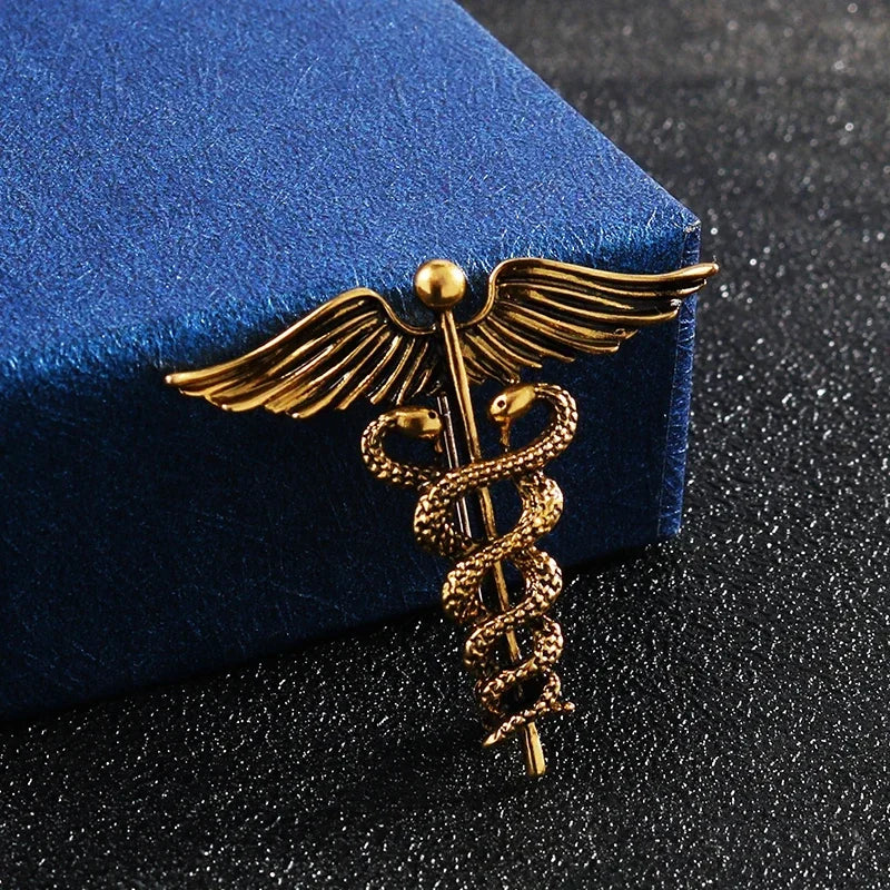 Gold caduceus brooch on a dark surface with a blue box in the background