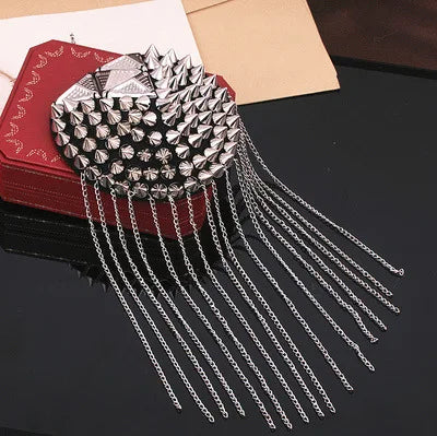 Silver spiked shoulder brooch with chain tassels on dark background