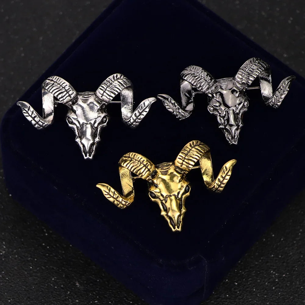 Gold and silver ram skull brooch pins displayed on a dark luxury background.