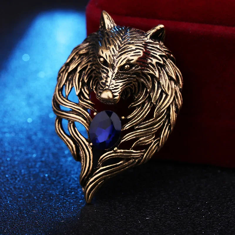 Gold wolf brooch with red gemstone on wooden surface background