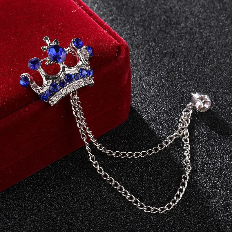 Crown-shaped brooch with blue gemstones on a chain, placed on a red velvet box.