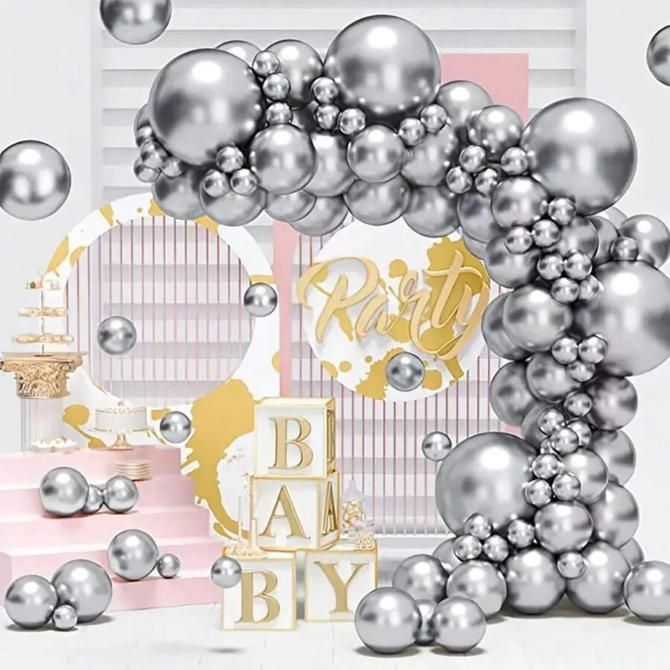 Silver and white balloon garland party decoration set with metallic silver balloons of various sizes, a gold and white arch backdrop, pink steps, and baby block letters spelling 'BABY'.