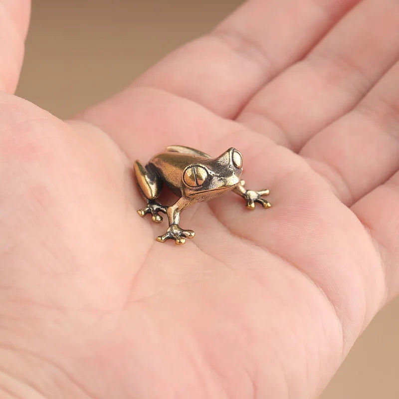 Bronze frog figurine held in a hand against a neutral background