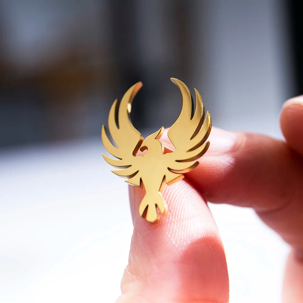Gold bird shaped earring held between fingers luxury fashion accessory close up