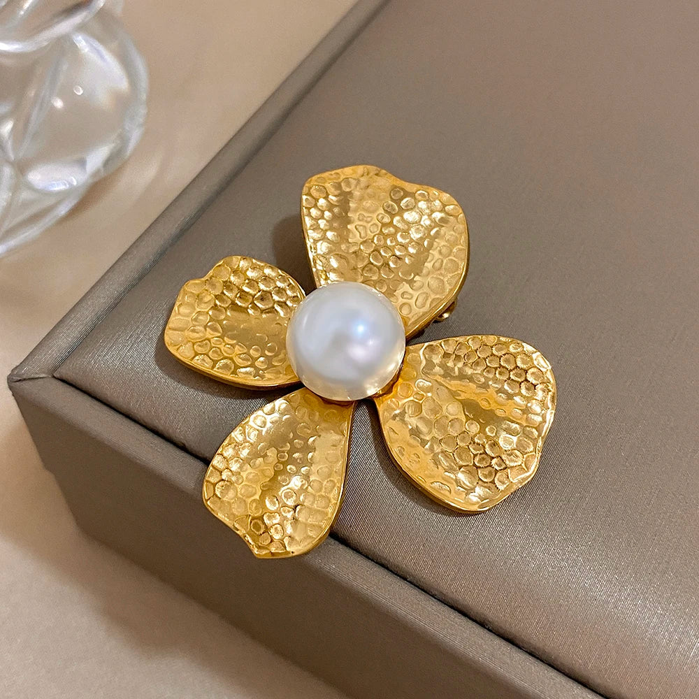 Gold flower-shaped brooch with a pearl center on a beige surface