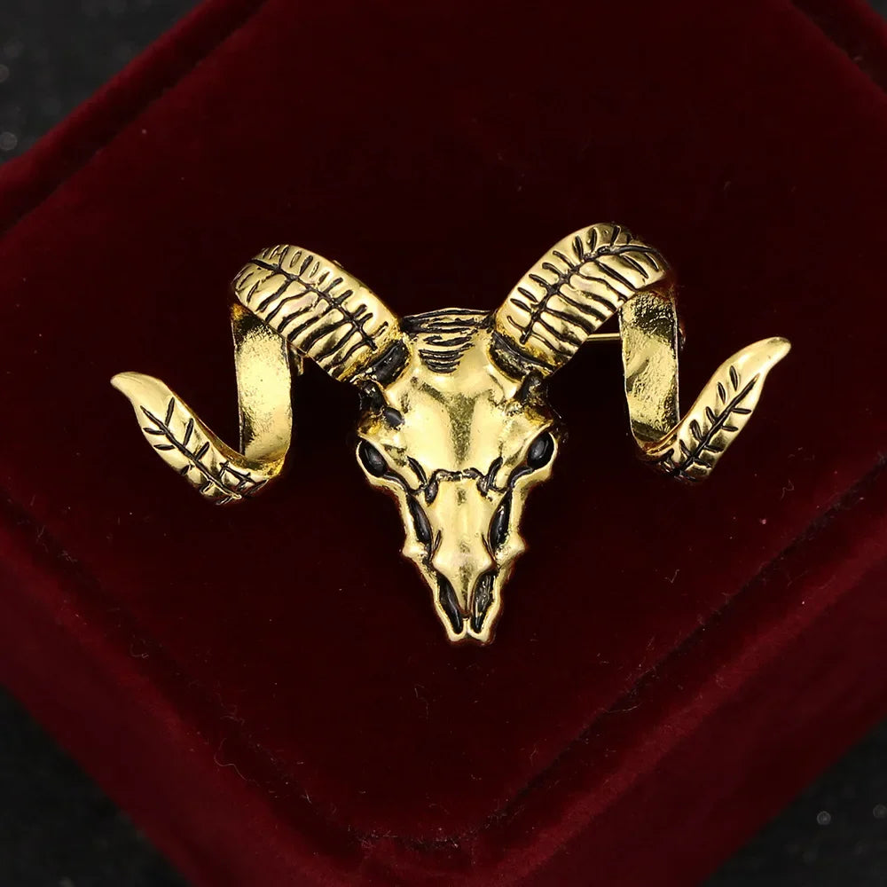 Gold ram skull brooch displayed on a luxury velvet jewelry stand.